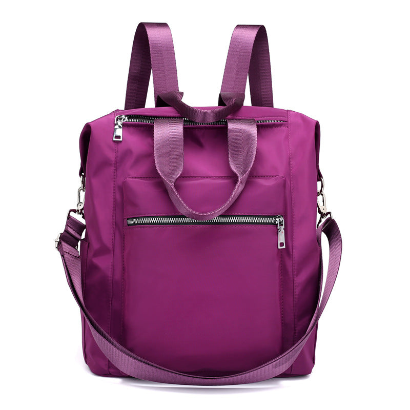 Purple nylon backpack with front zipper pocket, top handles, adjustable shoulder straps, and detachable crossbody strap