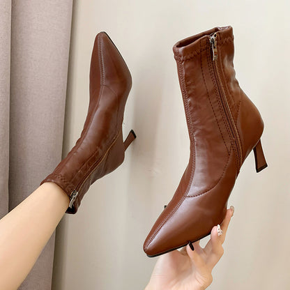 Brown leather ankle boots with side zipper and pointed toe, worn by person against neutral background