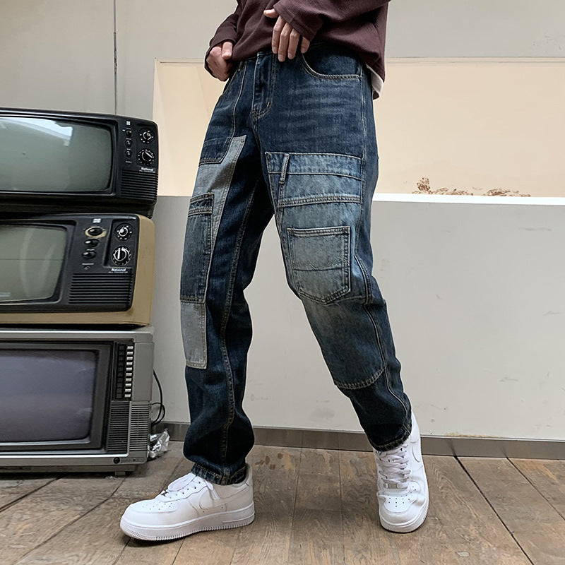 Person wearing dark wash patchwork denim cargo pants and white sneakers standing indoors near stacked vintage TVs