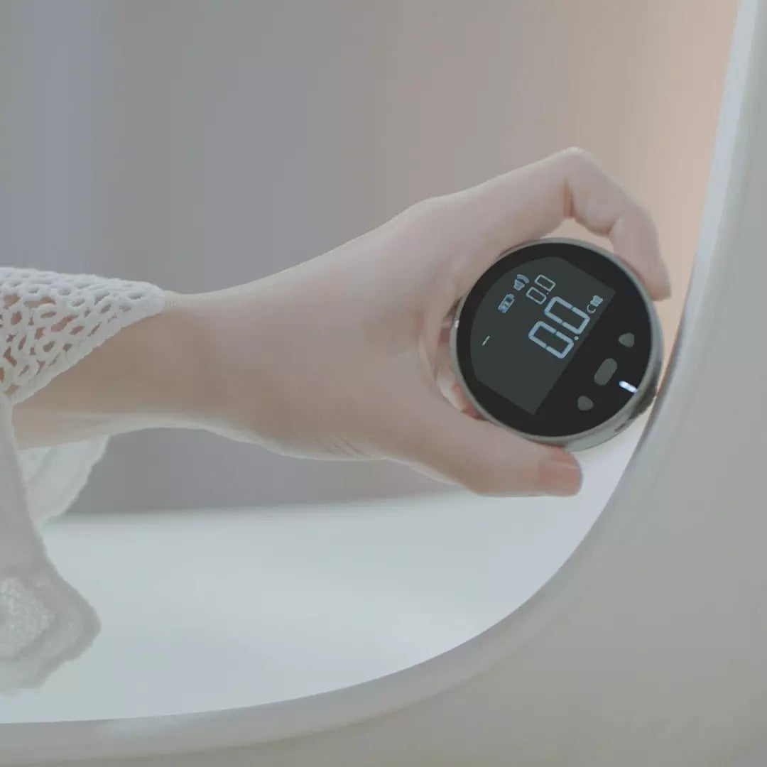 Hand holding a round digital device with a black screen displaying 0.0 in a soft white and beige setting