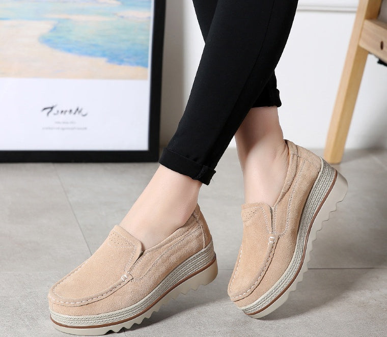 Beige suede platform slip-on shoes worn with black pants on tiled floor