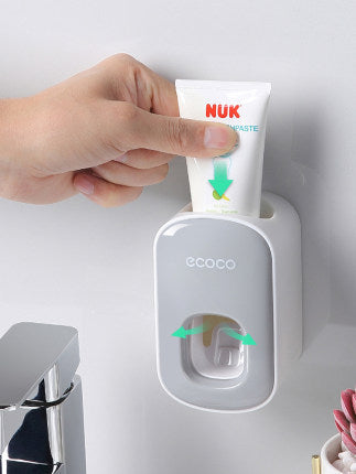 Hand pressing toothpaste tube into white Ecoco wall-mounted toothpaste dispenser in bathroom