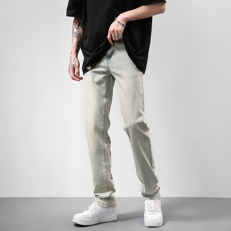 Man wearing light-wash slim fit jeans, white sneakers, and a black oversized T-shirt with tattoos on arm