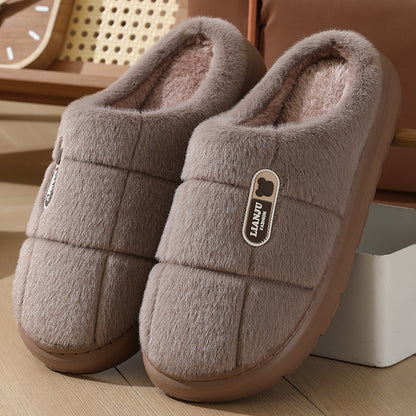 Plush brown indoor slippers with soft fleece lining and rubber sole on wooden floor