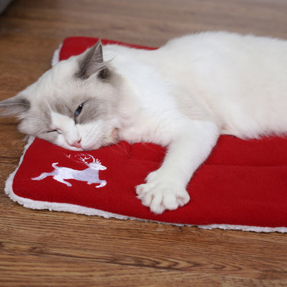 White and gray cat sleeping on red Christmas-themed pet mat with reindeer design on wooden floor