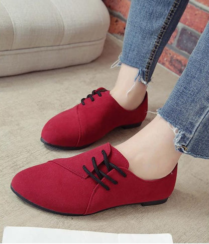 Close-up of red suede lace-up flat shoes worn with frayed hem blue jeans on concrete floor