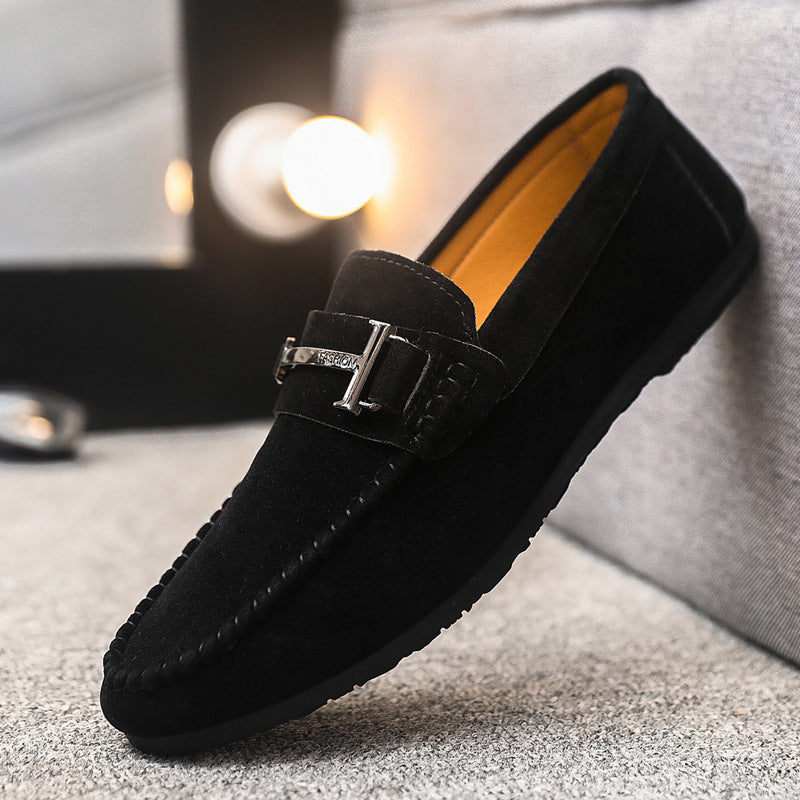 Black suede men's loafer with metal buckle detail and cushioned interior on gray fabric surface