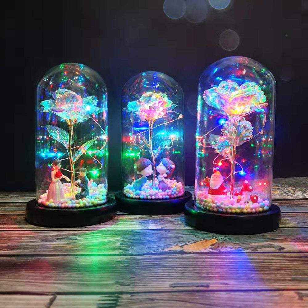 Three LED-lit glass domes with colorful roses and miniature figurines on wooden surface