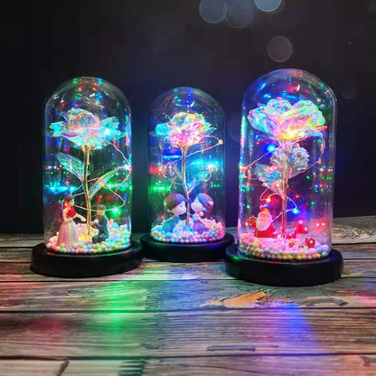 Three LED-lit glass domes with colorful roses and miniature figurines on wooden surface