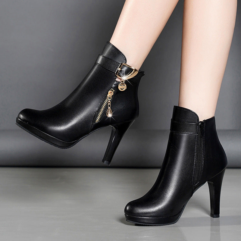 Black leather high-heeled ankle boots with gold zipper and buckle detail on model legs