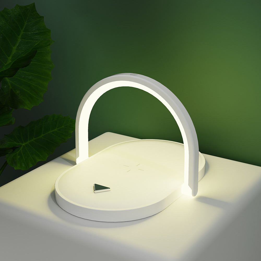 Modern white LED desk lamp with circular base and arch light on white table beside green plant