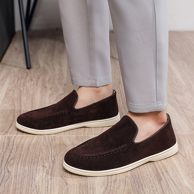 Men's casual slip-on brown suede shoes with white soles worn with light gray pants on wooden floor