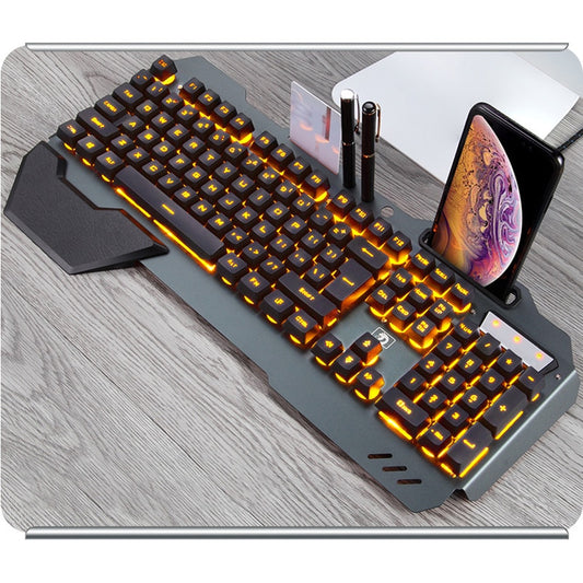 Gaming keyboard with orange backlight on wooden desk, phone and pens in integrated holder