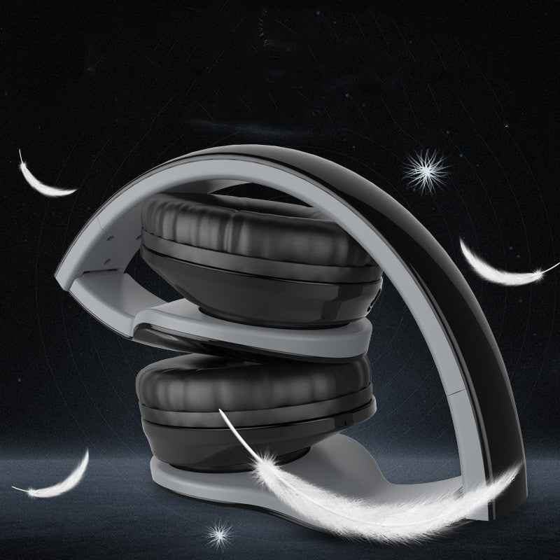 Foldable black wireless headphones with cushioned ear pads surrounded by floating white feathers