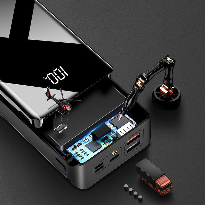 Black power bank with digital display, miniature helicopter, robotic arm, and small truck on dark surface
