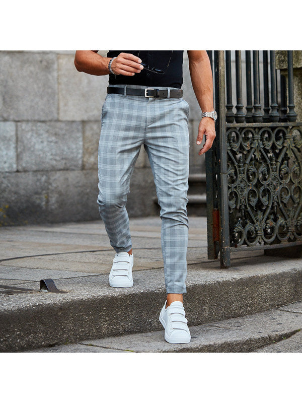 Man wearing gray plaid slim-fit pants and white sneakers walking on stone steps near a wrought iron gate