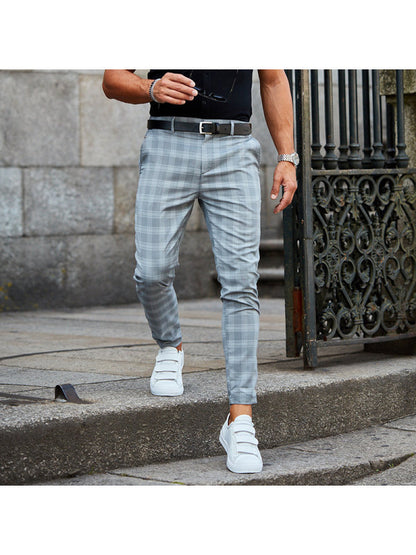 Man wearing gray plaid slim-fit pants and white sneakers walking on stone steps near a wrought iron gate