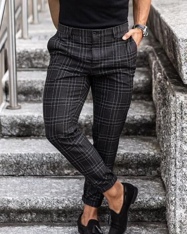 Man wearing black and gray plaid slim-fit trousers with black loafers standing on stone steps