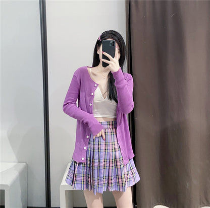 Woman taking mirror selfie wearing purple cardigan, beige crop top, and purple plaid pleated skirt