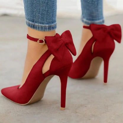 Red high heel shoes with ankle straps and large bows on back, worn with rolled-up jeans