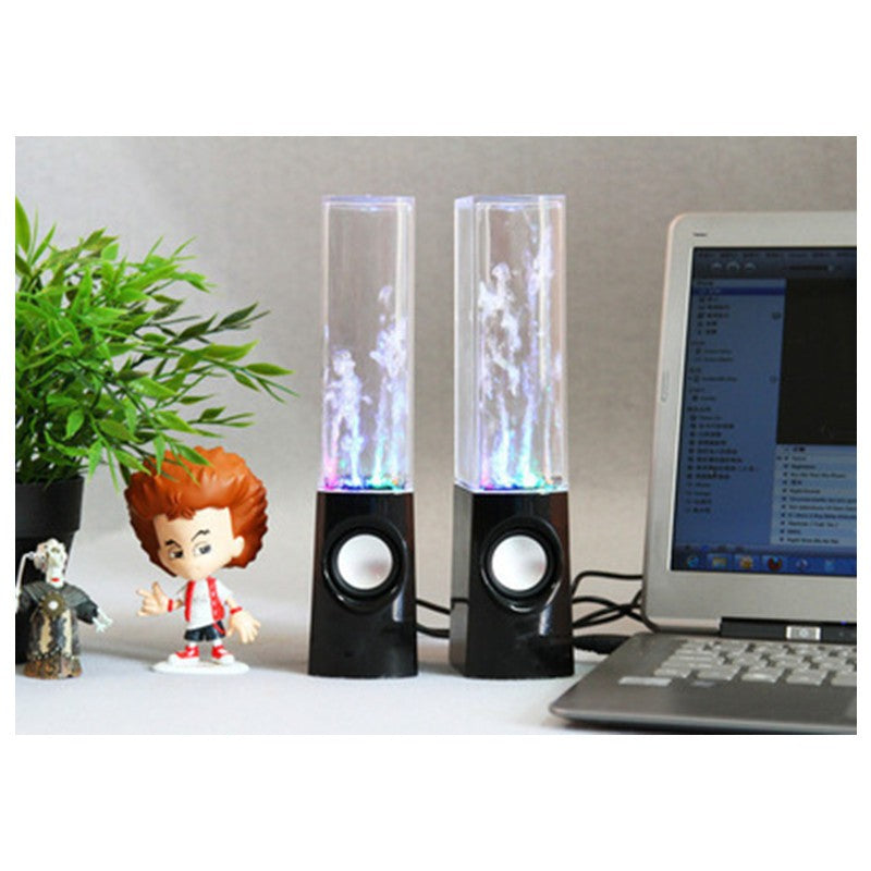 Colorful water dancing speakers on desk next to laptop, toy figures, and green plant