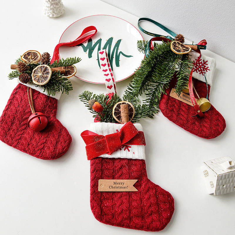 Three red knitted Christmas stockings decorated with greenery, pinecones, dried orange slices, and festive ribbons on a white surface