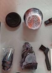 Disassembled electric hair clipper with detachable blades, comb, brush, and lubricating oil on gray surface