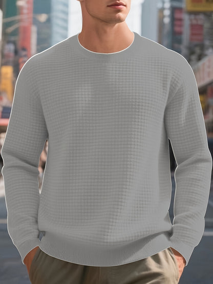 Man wearing light gray textured knit sweater with round neck and hands in pockets in urban street setting
