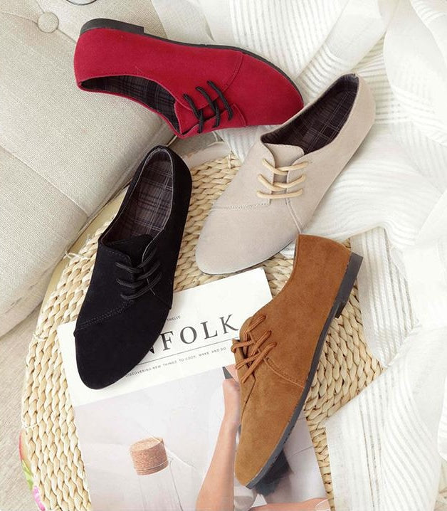 Four pairs of suede lace-up ankle boots in red, beige, black, and brown on a woven mat with a Kinfolk magazine