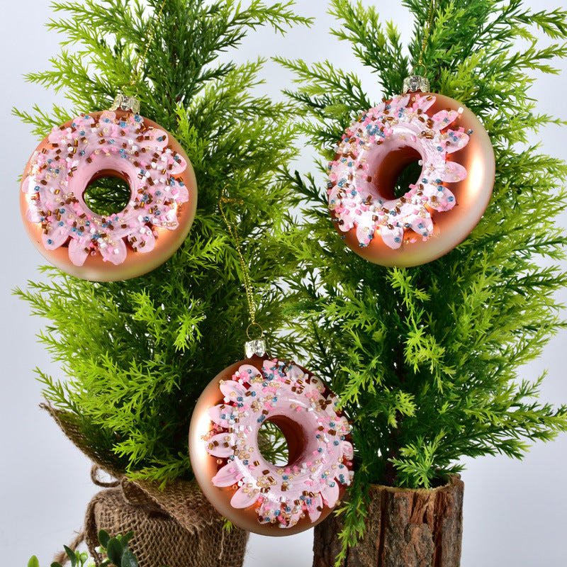 Three pink frosted donut Christmas ornaments with sprinkles hanging on green pine branches