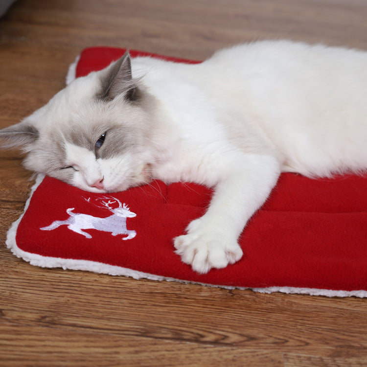 White and gray cat lying on a red festive mat with a white reindeer design on wooden floor