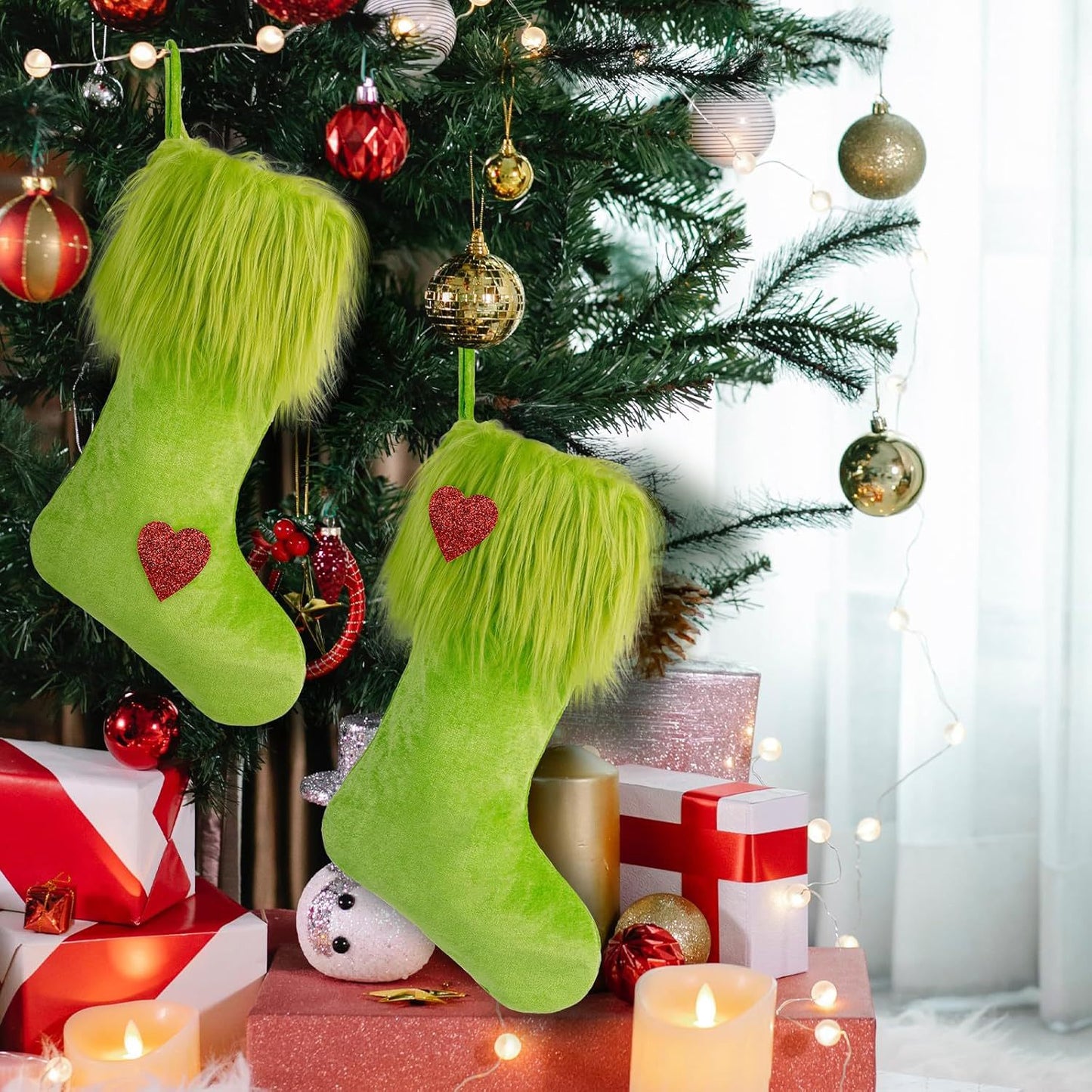 Two green fuzzy Christmas stockings with red heart patches hanging on a decorated tree with red and gold ornaments