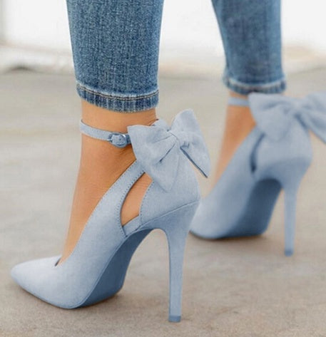 Light blue suede high heels with ankle straps and large bows, worn with rolled-up skinny jeans