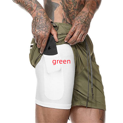 Tattooed man wearing green athletic shorts with white compression pocket holding black smartphone