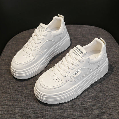 Pair of white platform sneakers with laces and visible FASHION labels on grey fabric surface