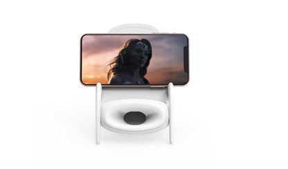 White phone stand with Bluetooth speaker holding smartphone playing movie scene with woman at sunset