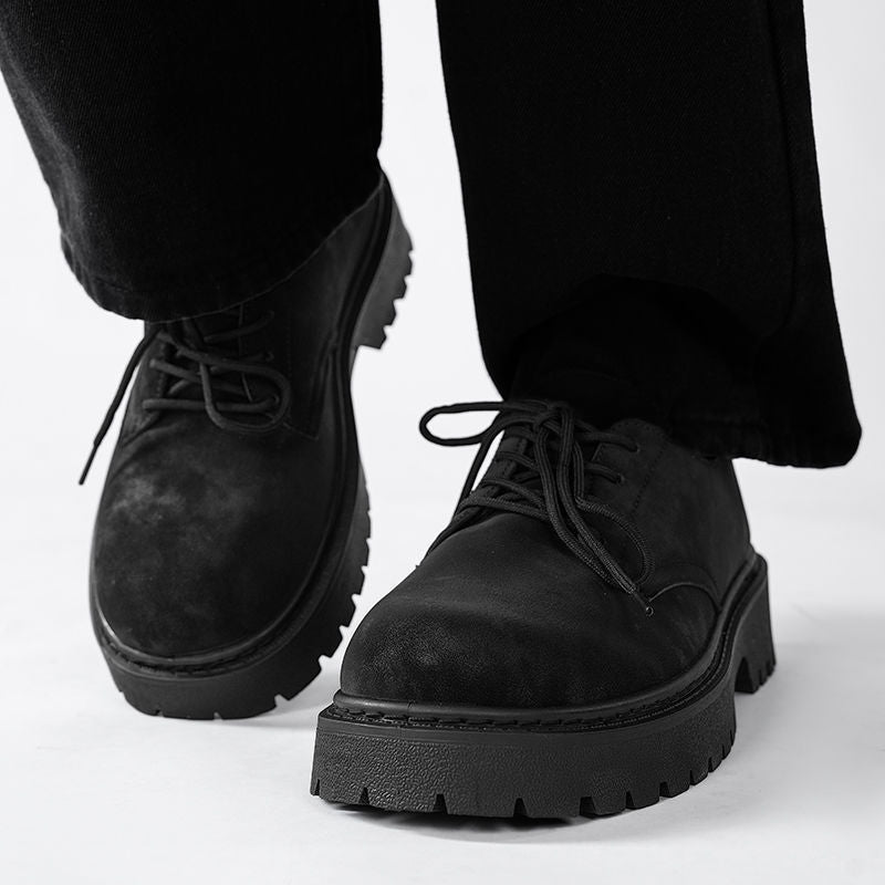 Close-up of black leather lace-up platform shoes with rugged soles worn with black pants