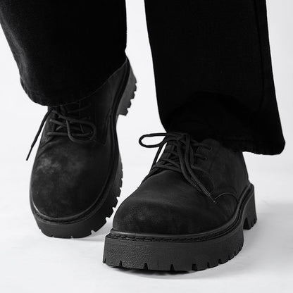 Close-up of black leather lace-up platform shoes with rugged soles worn with black pants