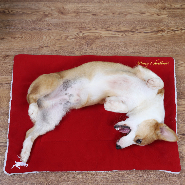 Corgi dog lying on red Christmas-themed mat on wooden floor, playful pose