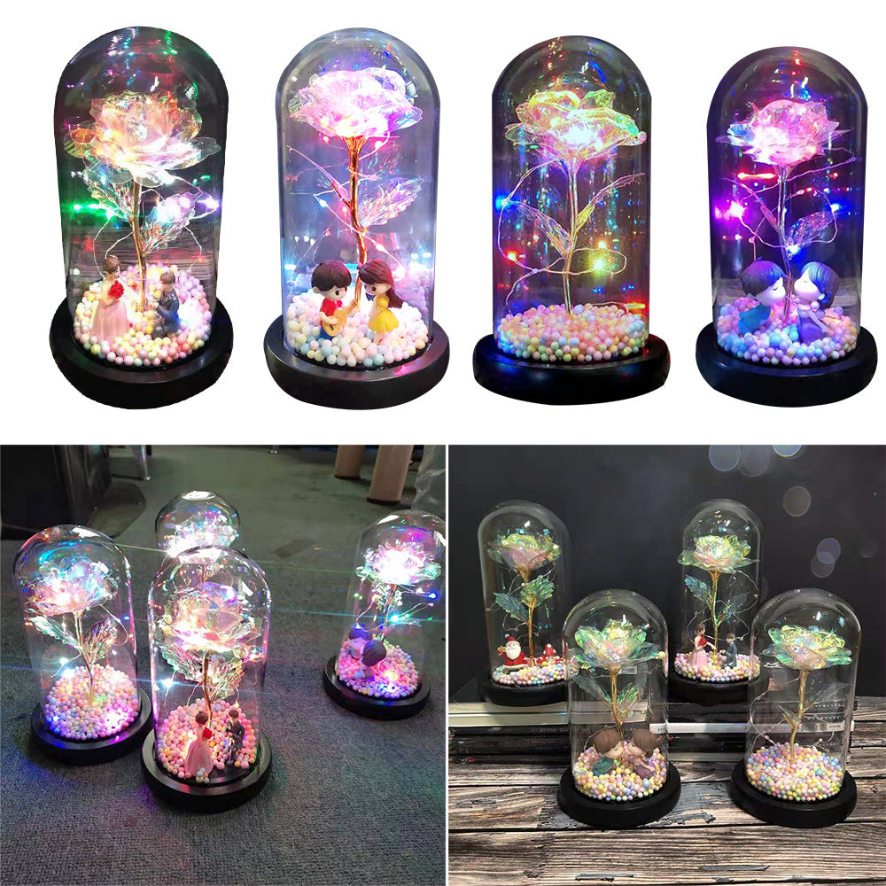 Decorative glass domes with glowing roses and miniature couples inside on black bases with LED lights