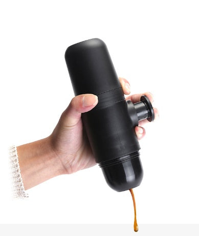 Hand holding a black portable espresso maker with coffee pouring out against a white background