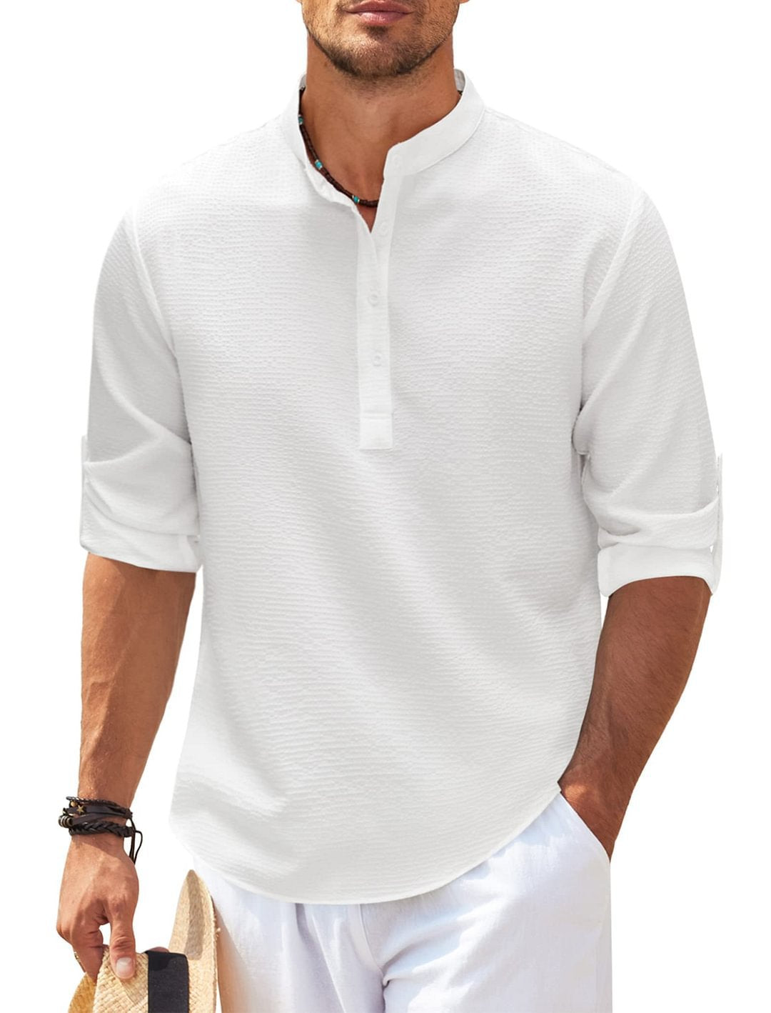 Man wearing white textured long sleeve henley shirt with rolled cuffs and white pants holding straw hat