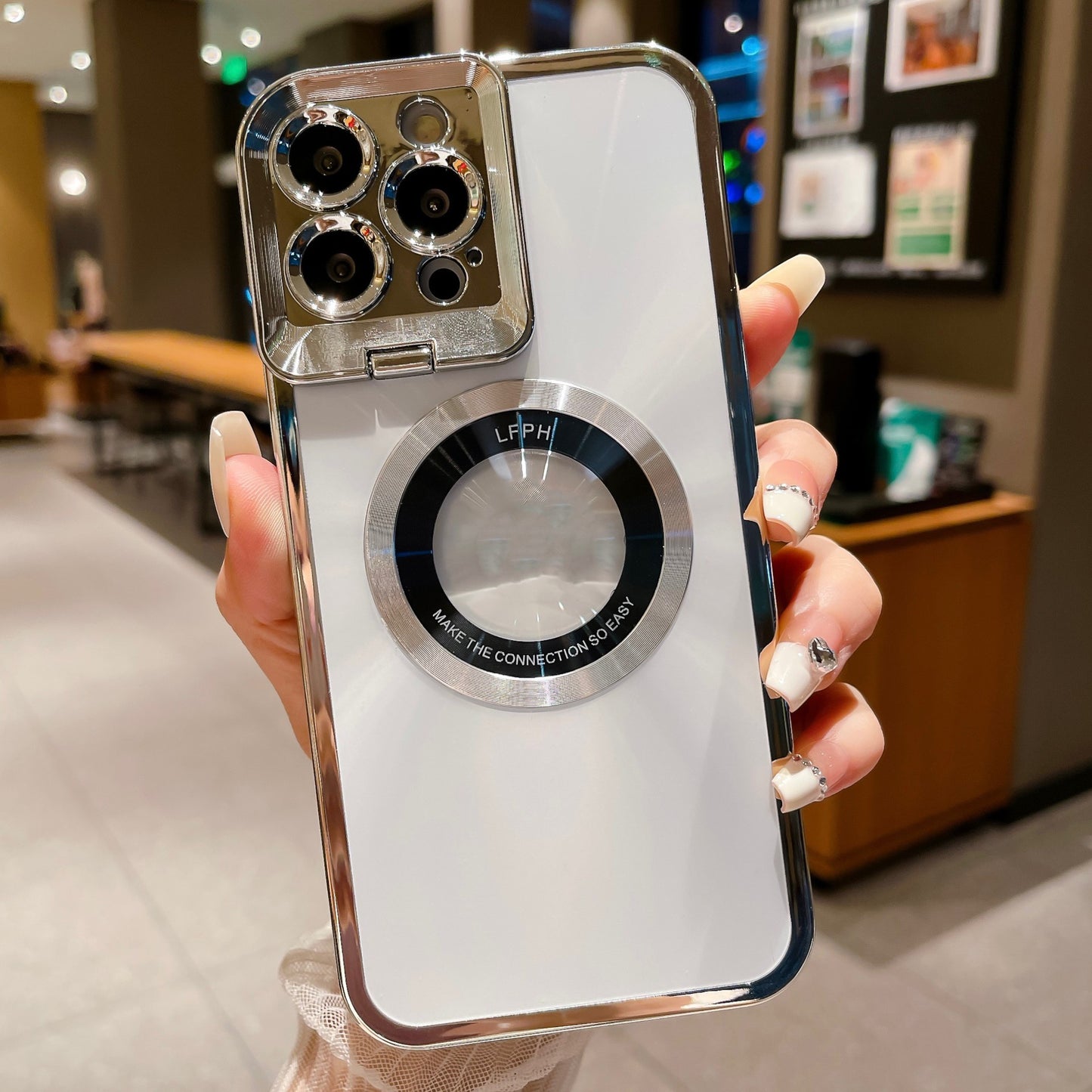 Hand holding a white smartphone with a clear case featuring triple camera lenses and a circular magnet ring