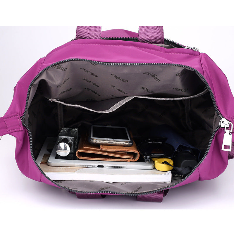 Open purple handbag showing organized interior with wallet, smartphone, sunglasses, tablet, and small items