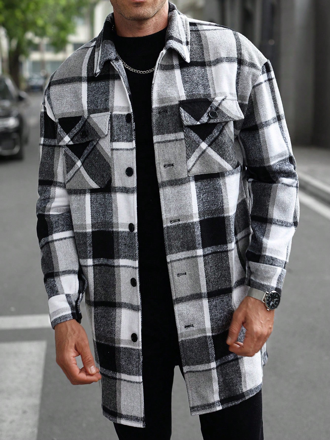 Man wearing black white gray plaid button-up shirt jacket with long sleeves on city street