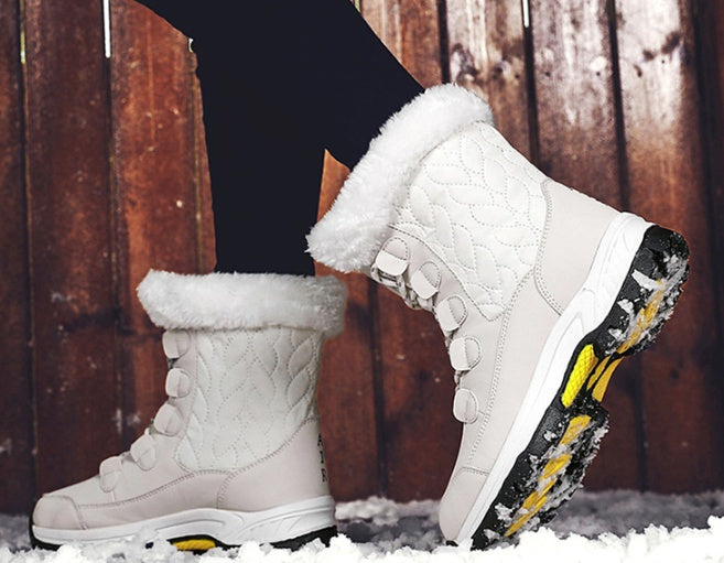 White quilted winter boots with faux fur trim and black-yellow slip-resistant soles on snowy ground
