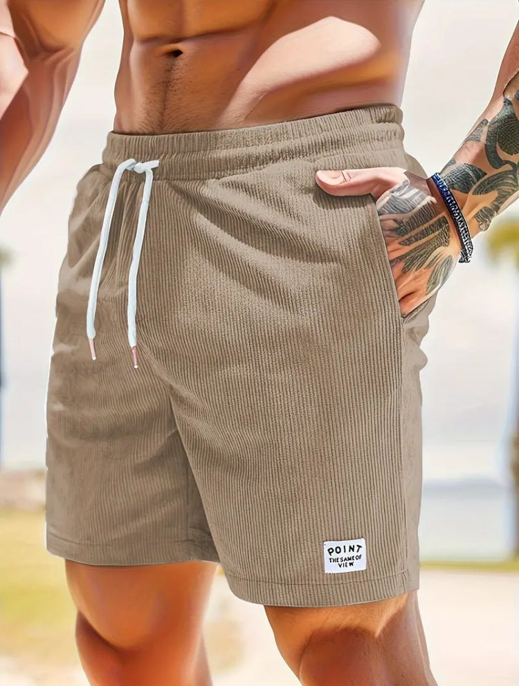 Close-up of muscular man wearing beige ribbed drawstring shorts with tattooed arm and bracelet