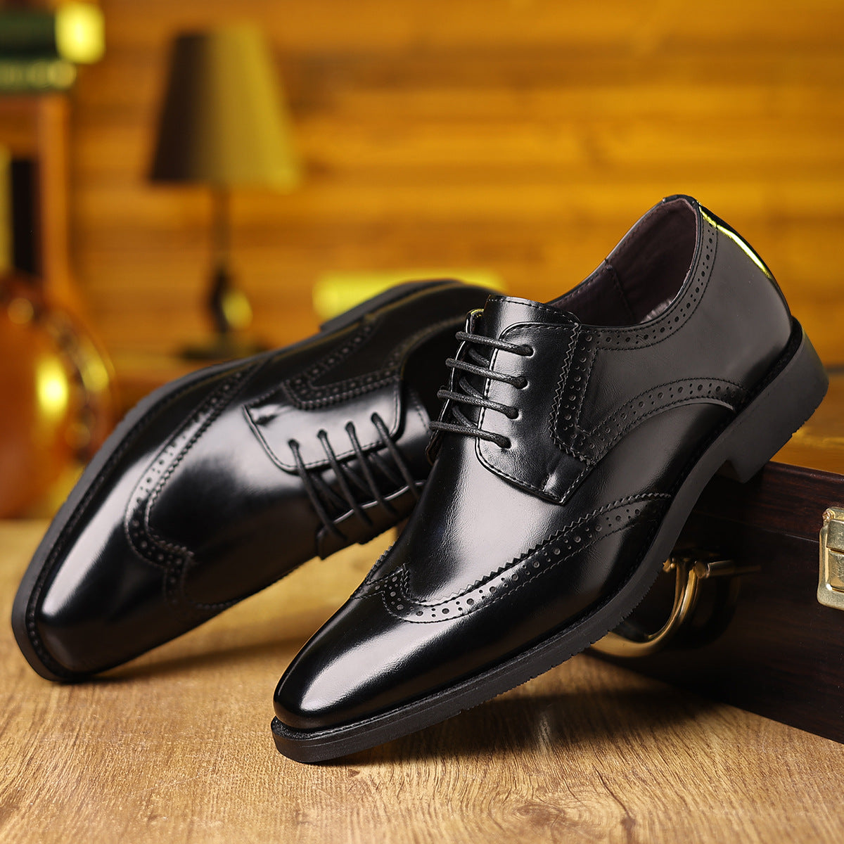 Pair of polished black leather men's dress shoes with brogue detailing on wooden surface