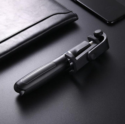 Black foldable selfie stick with textured grip on a dark surface near black leather folder