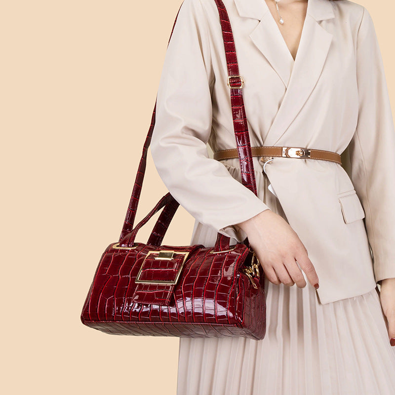 Woman in beige blazer and pleated skirt holding red crocodile texture leather handbag with gold buckle